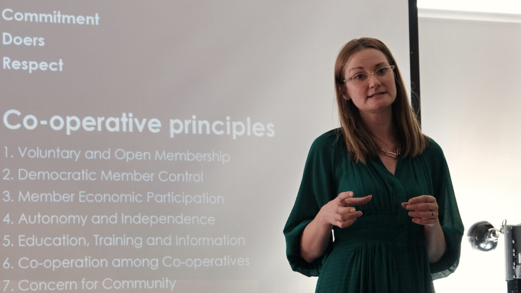 Woman presenting and standing next to text on a presentation that reads "Co-operative principles."