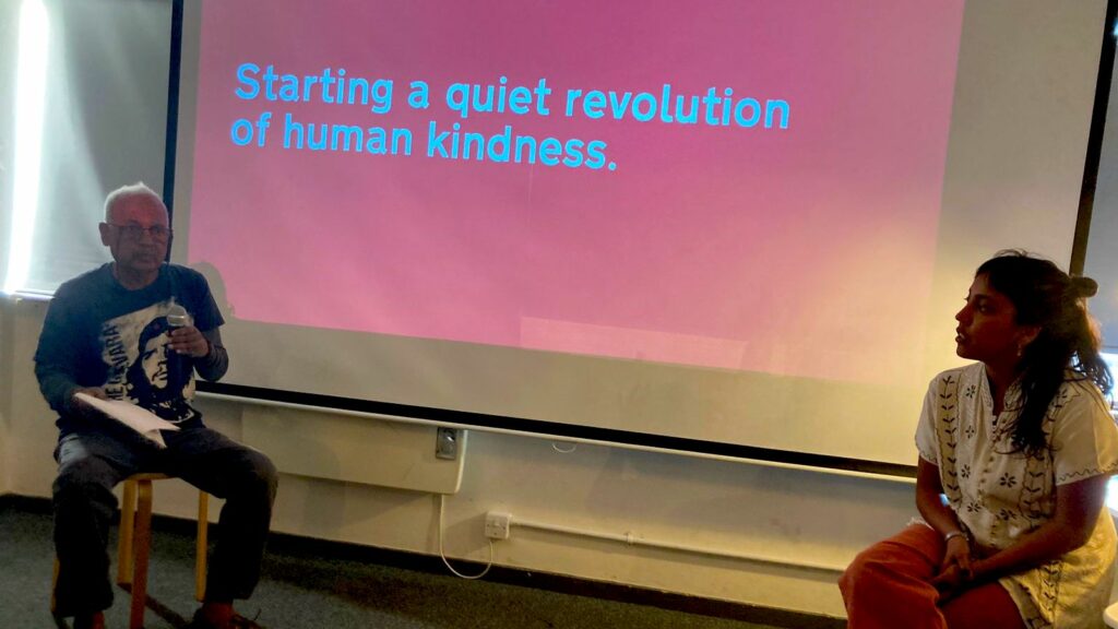 Image of Alagarathnam speaking at SPACE4. Slide on the presentation says "Starting a quiet revolution of human kindness."